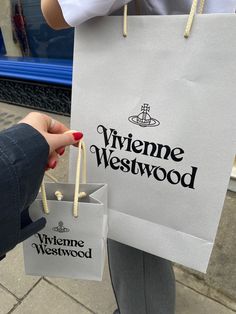 a woman is holding two shopping bags with the name viviene westwood on them