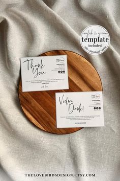 two business cards sitting on top of a wooden plate next to a white linen covered bed