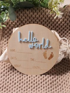 a wooden sign that says hello world with baby footprints on it and flowers in the background