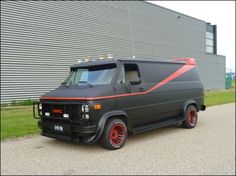 a van parked in front of a building with red rims on it's tires