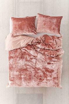 a bed covered in pink velvet with two pillows on top of it and a pillow case