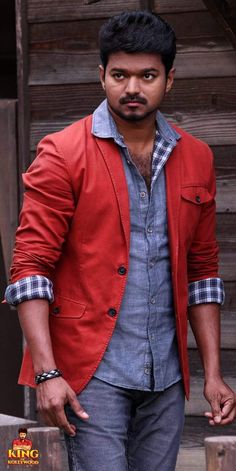 a man standing in front of a wooden building wearing a red jacket and blue shirt