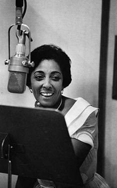 a black and white photo of a woman sitting in front of a microphone with a laptop on her lap