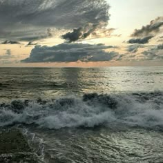 the sun is setting over the ocean with some clouds in the sky and waves crashing on the shore