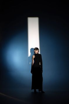 a woman is standing in the dark with her back turned to the camera and she's wearing a black dress