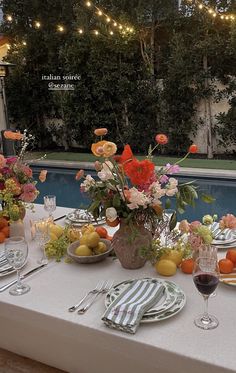 an outdoor table set with flowers and fruit by the pool for a party or dinner