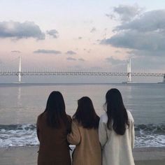 three women standing on the beach looking out at the water and bridge in the background