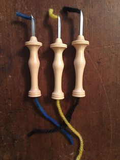 three small wooden candlesticks with blue and yellow cords attached to them on a wood surface