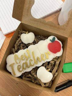 an open box with some cookies in it on top of a wooden table next to writing utensils