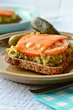 an open face sandwich with tomato and avocado on toasted bread, next to pickles