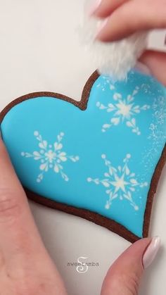 someone is decorating a heart shaped cookie with icing and snowflakes on it