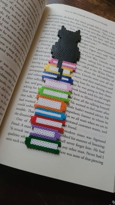 a cross stitch bookmark made to look like a black bear sitting on top of a pile of books