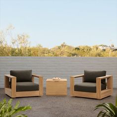 two chairs and a coffee table sitting in front of a white brick wall with trees