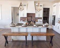 a kitchen with white cabinets and an island in the middle, two wooden benches at the center