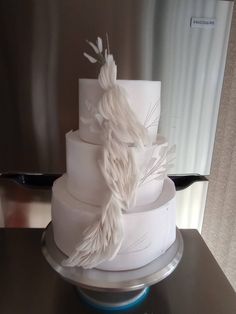 a three tiered white cake with feathers on top