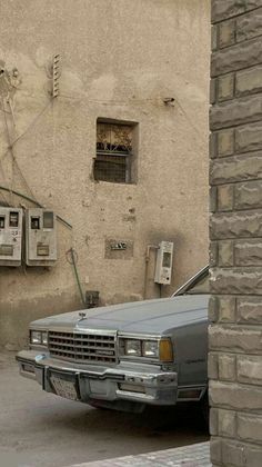 an old car parked in front of a building with two telephones on the wall