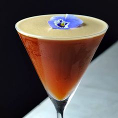 a martini glass with an orange liquid and a blue flower