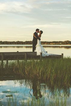 a bride and groom standing on a dock by the water