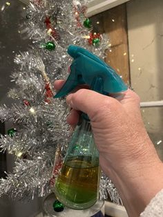 a person is holding a spray bottle near a christmas tree