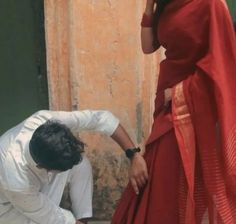 a man kneeling down next to a woman in a red dress and white shirt on her cell phone