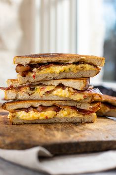 a stack of four sandwiches sitting on top of a wooden cutting board