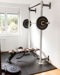 a gym room with a bench, barbells and weight plates on the floor