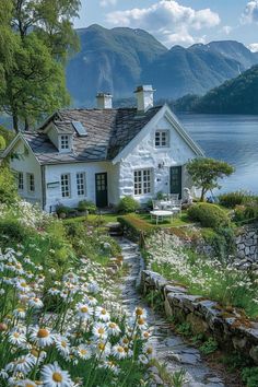 a white house sitting on top of a lush green hillside next to a body of water