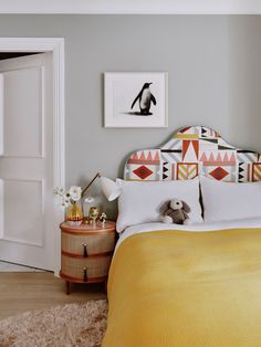 a bedroom with yellow and white bedding, pictures on the wall and a teddy bear