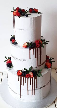 a three tiered cake with strawberries and chocolate drizzled on top