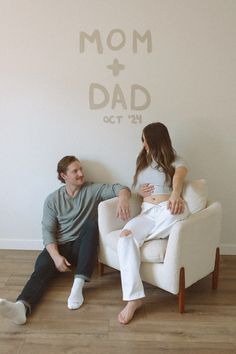 a man and woman sitting on a chair in front of a wall with the words mom and dad painted on it