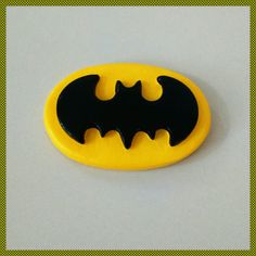 a yellow and black batman button on a white surface