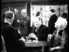 an old man and woman sitting at a table in a bar talking to each other