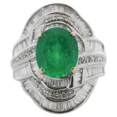 Remarkable in craftsmanship and design, this gorgeous 18k white gold emerald and diamond ring is undeniably unique. An oval cut fine quality emerald sits in the center secured in a prong setting with a weight of 3.89 carats and measures 11.1 X9.3MM. This emerald is complemented by 3.56 carats of shimmering baguette and round brilliant cut diamonds, all channel and prong set in a cascading cluster of brilliance and fire.