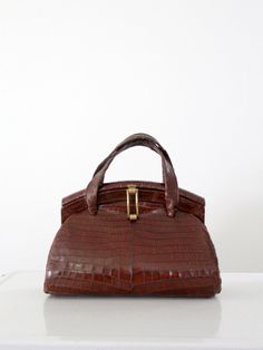 This is a vintage alligator purse from the late 1950s. The large frame top bag features double top handles, brass fixtures, and a black lined interior with side pockets. CONDITION In good condition with wear consistent with age and use. There is some wear around the handles and corners. MEASUREMENTS Height: 8.5 inch ... 21.6 cm Length: 13 inch .. 33 cm Width: 6 inch .. 15.2 cm Handle drop: 4 inch .. 10.2 cm 51332 Alligator Purse, Alligator Handbags, Hippie Boots, Brass Fixtures, Brown Leather Handbags, Top Handle Bags, Vintage Purses, Vintage Handbags, Vintage Bags