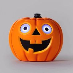 an orange halloween pumpkin with eyes and mouth is shown in front of a gray background