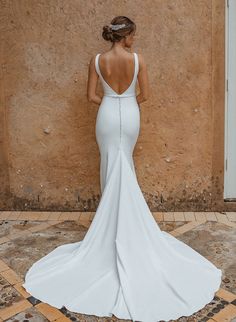 the back of a woman in a white wedding dress, standing against a stone wall