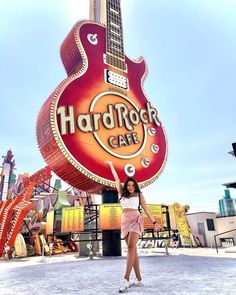 a woman standing in front of a guitar shaped sign with the word hard rock cafe on it