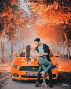 a man and woman sitting on the hood of an orange car with trees in the background