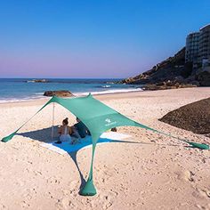 two people are sitting under a tent on the sand at the beach by the ocean