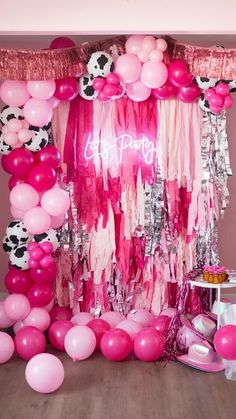 a pink and white birthday party with balloons, streamers and cow print decorations on the wall