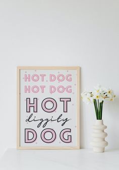 a white vase with flowers sitting on top of a table next to a sign that says hot dog