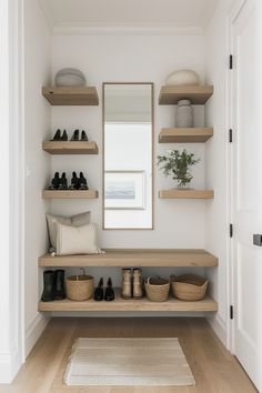 a white hallway with wooden shelves and shoes on the floor next to a large mirror