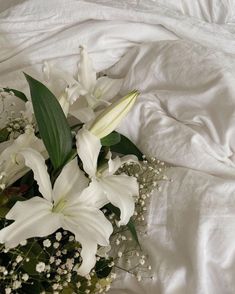 a bouquet of white lilies and baby's breath sits on a bed sheet