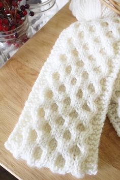 a crocheted scarf sitting on top of a wooden table next to a bowl of pomegranates