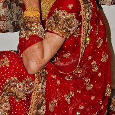 a woman in a red sari sitting down with her hands on her face and wearing gold jewelry