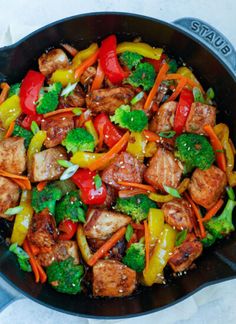 a skillet filled with chicken, broccoli, peppers and carrots on top of a stove