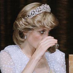 a woman wearing a tiara drinking out of a cup while sitting at a table