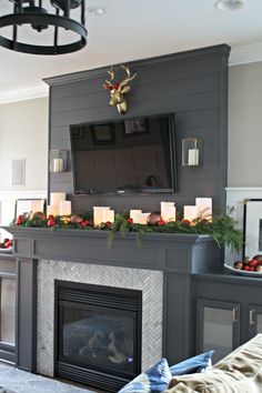 a living room decorated for christmas with candles on the mantel and a television mounted above it