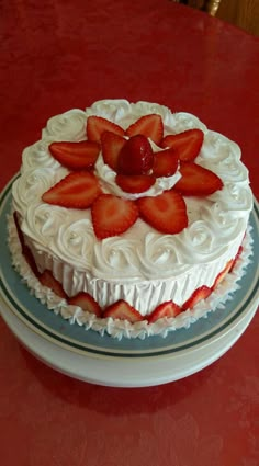 there is a cake with white frosting and strawberries on the top, sitting on a plate