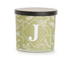 a candle that is sitting in front of a white and green background with the letter j on it